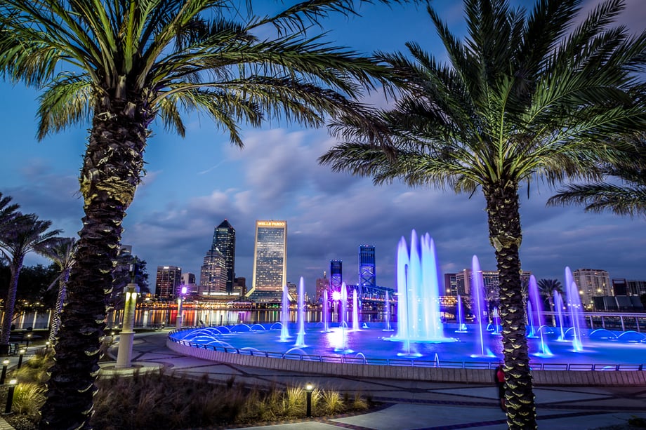 Two palm trees in front of a lit-up fountain overlooking the city of Jacksonville at dusk