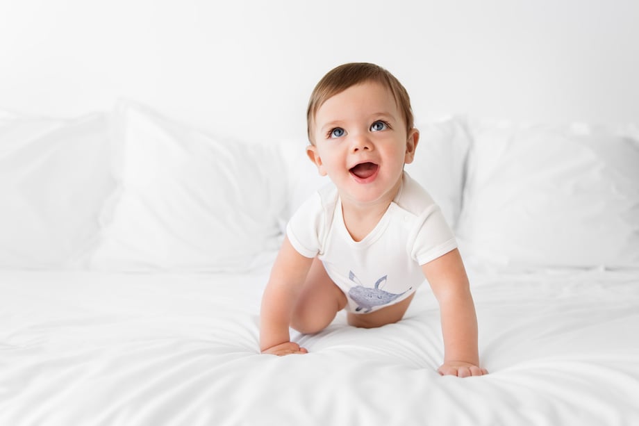 Photograph of a baby in Olivia Yves onesie crawling on a bed.