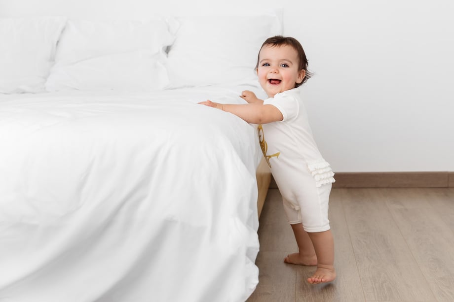 Photograph of a baby in Olivia Yves clothing holding onto a bed.