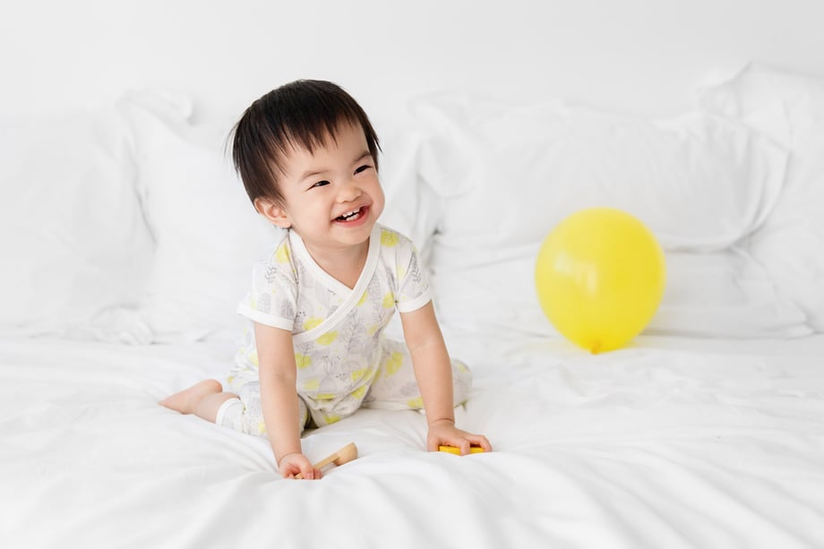 Photograph of a baby on a bed with toys next to a balloon.