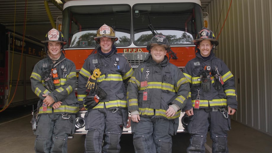 Four firefighters in gear stand in front of a fire truck in this photo by Josh LeClair