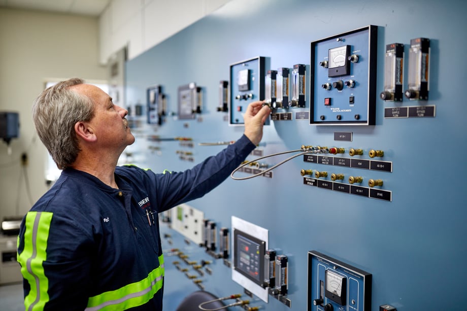 Adrian Baird catches a shot of an employee standing before a monitoring wall full of dials and switches