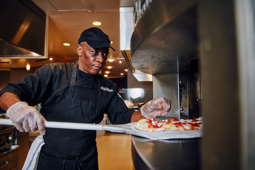 Photograph of a chef putting a pizza in a brick oven. 