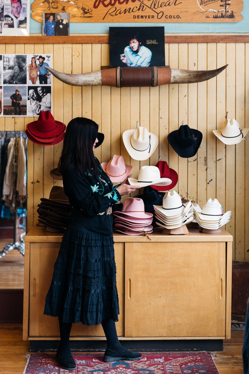 Photo shows a woman in black admiring a display of cowboy hats