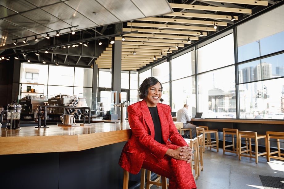 Sara Stathas' photo of Roz Brewer in a red suit, sitting with her legs crossed at the Starbucks counter