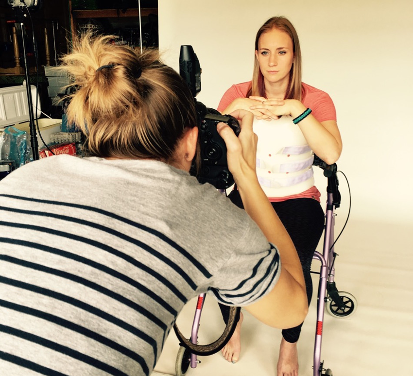 Behind-the-scenes photo of Sara photographing Amber Hohnhorst, a survivor of a hiking accident, while sitting in a walker, wearing a back brace