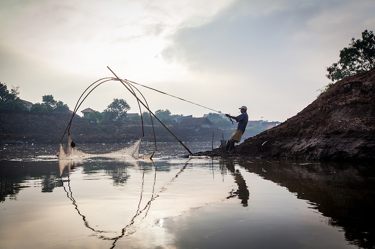 Photograph of a man strains as he pulls his fishing net out of the polluted water of the Citarum River for Greenpeace.
