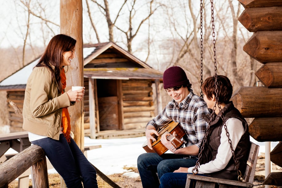 Lifestyle image showing three friends on the porch of a cabin, one playing a guitar