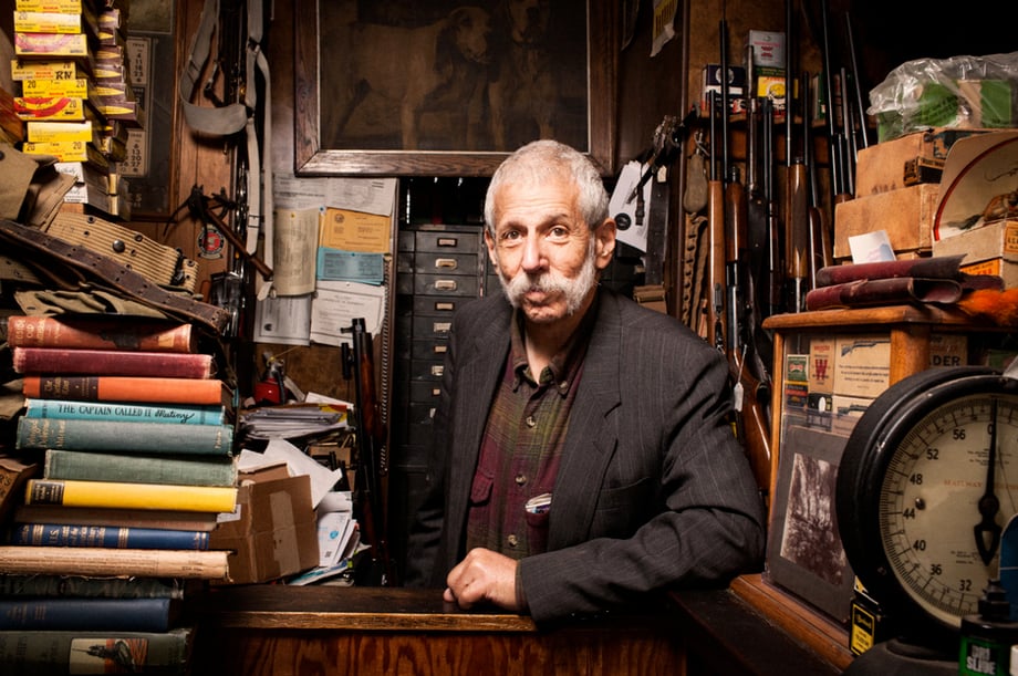 A portrait of an older man surrounded by books and other objects photographed by Seth Lowe