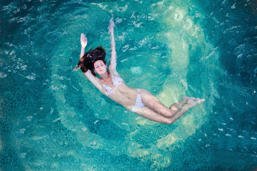aerial photography showing a woman posing with her arms over her head, while floating in a pool