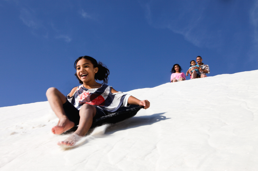 lifestyle photography of a young girl sledding while her family watches