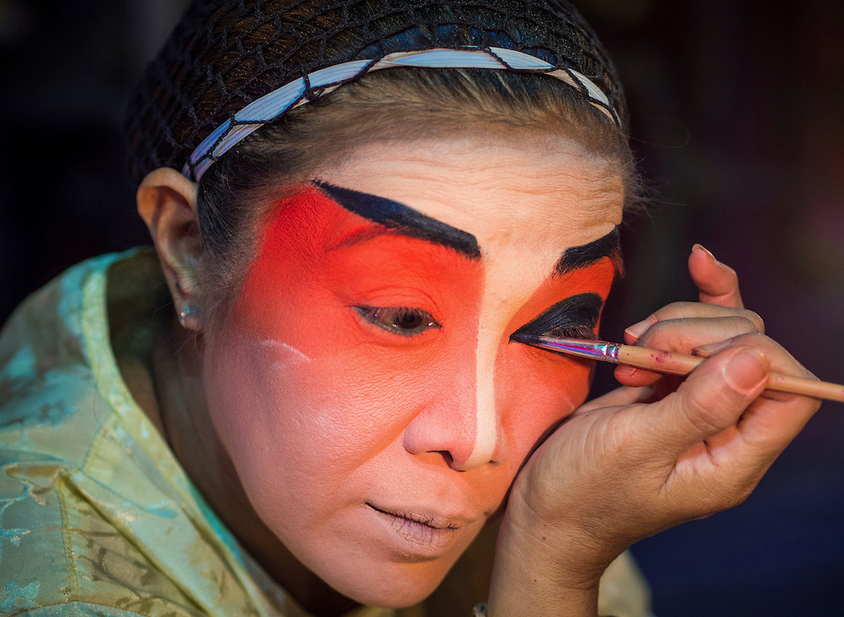 A member of the Lehigh Leng Kaitoung Opera troupe applies her makeup before a performance at Chaomae Thapthim Shrine photographed by Jack Kurtz