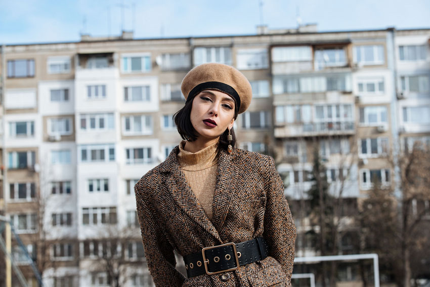 Victoria in a brown suit and beret standing in front of her Bulgarian childhood home