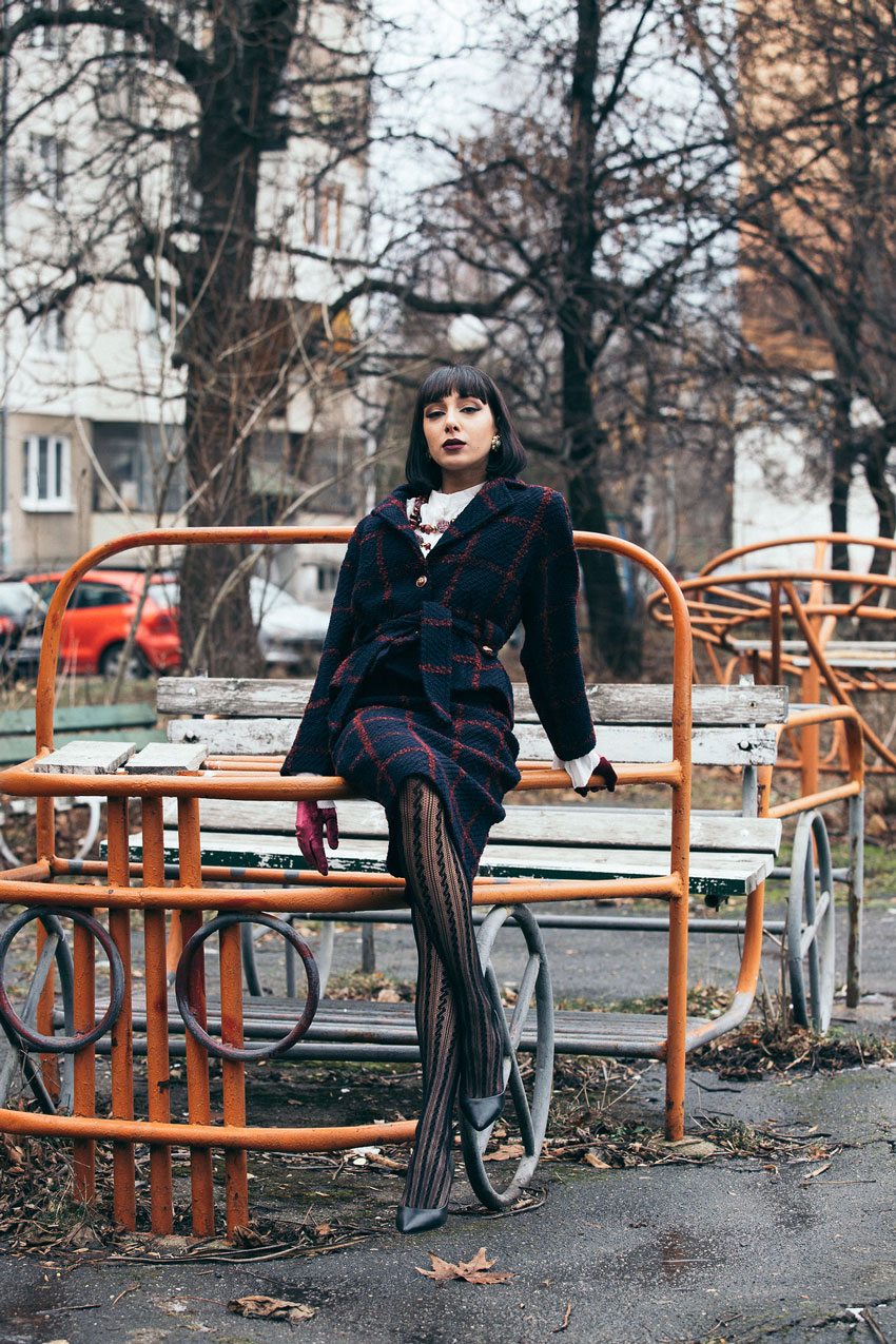 Victoria in a navy suit and heels, leaning on an unsafe playground structure in Bulgaria