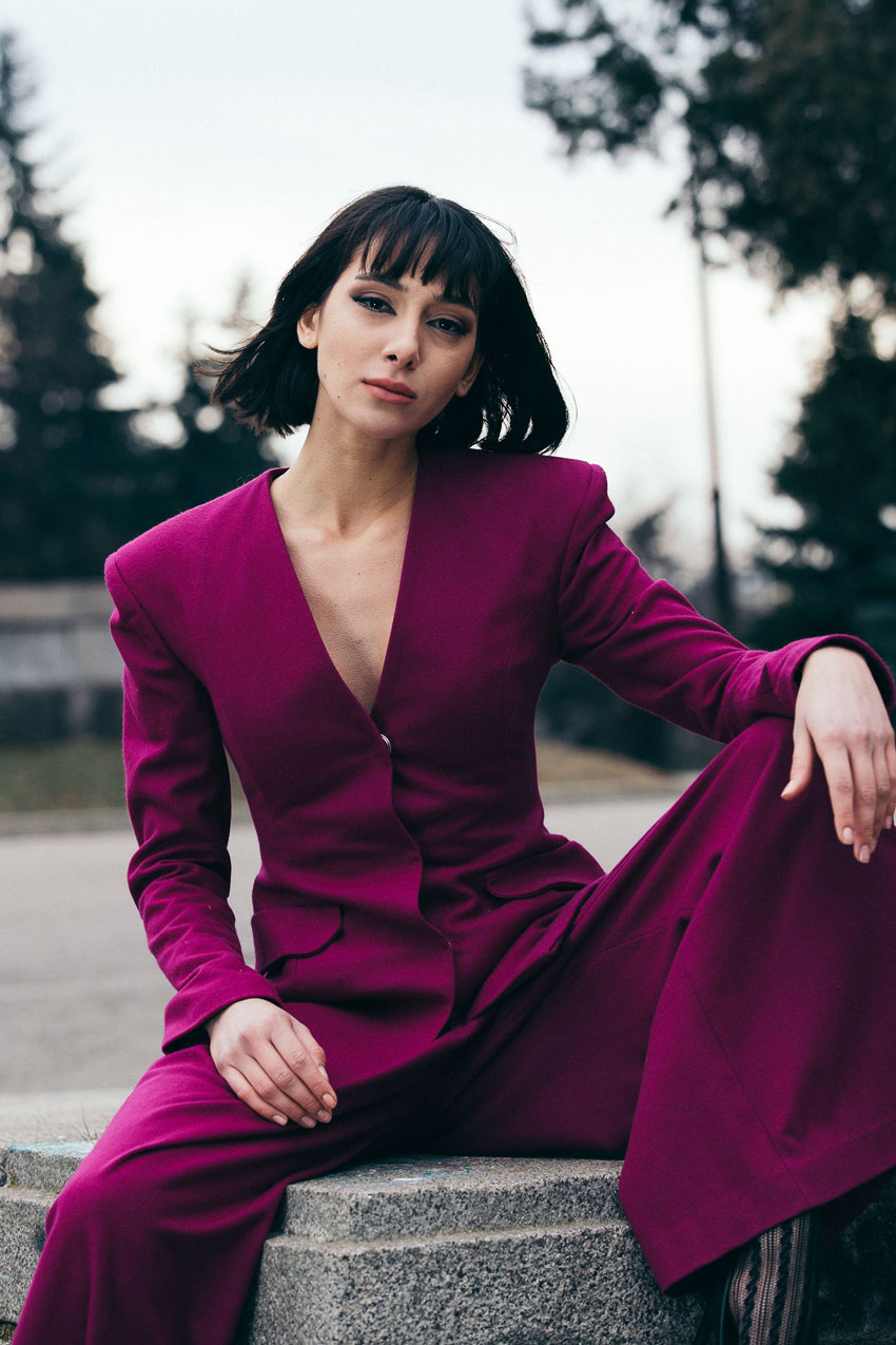 Tina Boyadjieva's close up of a model in a bright purple suit sitting on a monument in Bulgaria