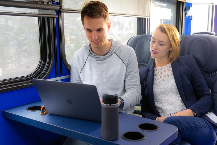Steve Boxall's photo of a young man and woman sit side by side, looking at a laptop while sitting in an electric bus