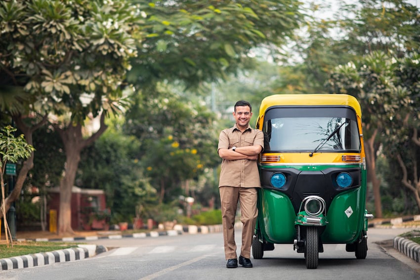 An UBER driver stands next to his green and yellow auto rickshaw in this photo by Felix Reed