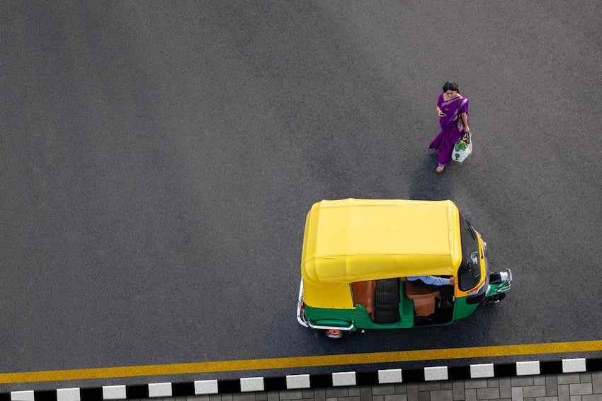 A young woman carrying a bag of groceries walks towards an UBER auto rickshaw in this aerial shot by Felix Reed