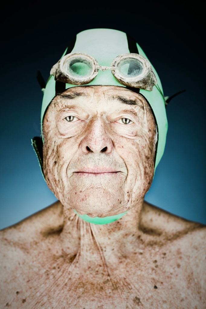 Photo of an older male swimmer in a green cap staring into the camera.