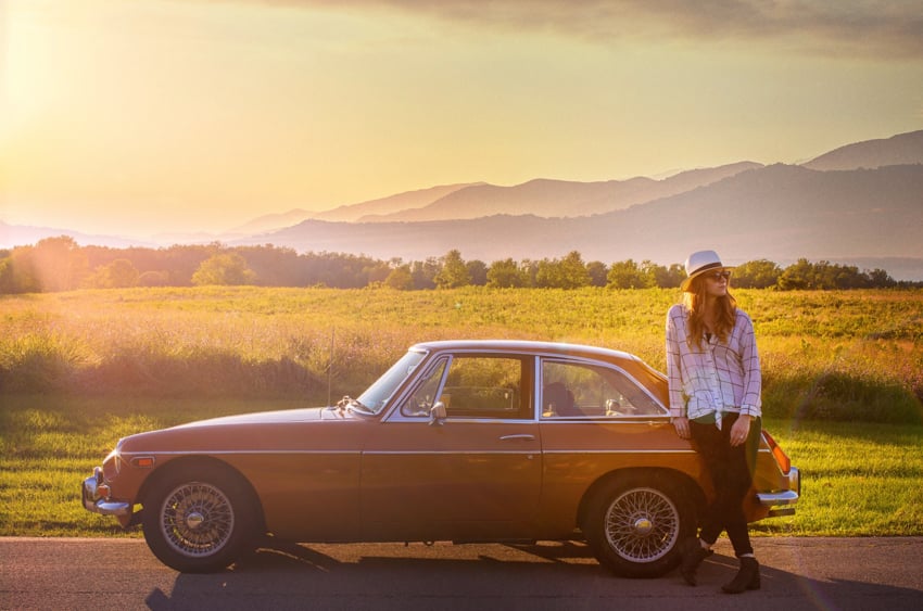 Will Strawser photographs a young woman leaning against an old car with mountains in the distance.