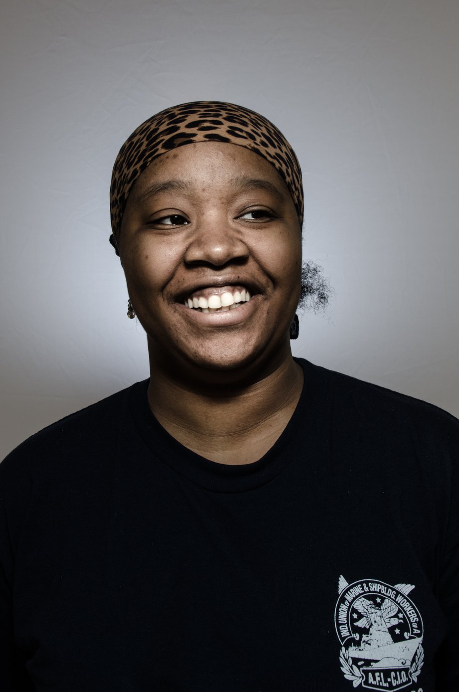 Heather Perry's portrait of Amanda, smiling, in a black t-shirt and leopard print head wrap