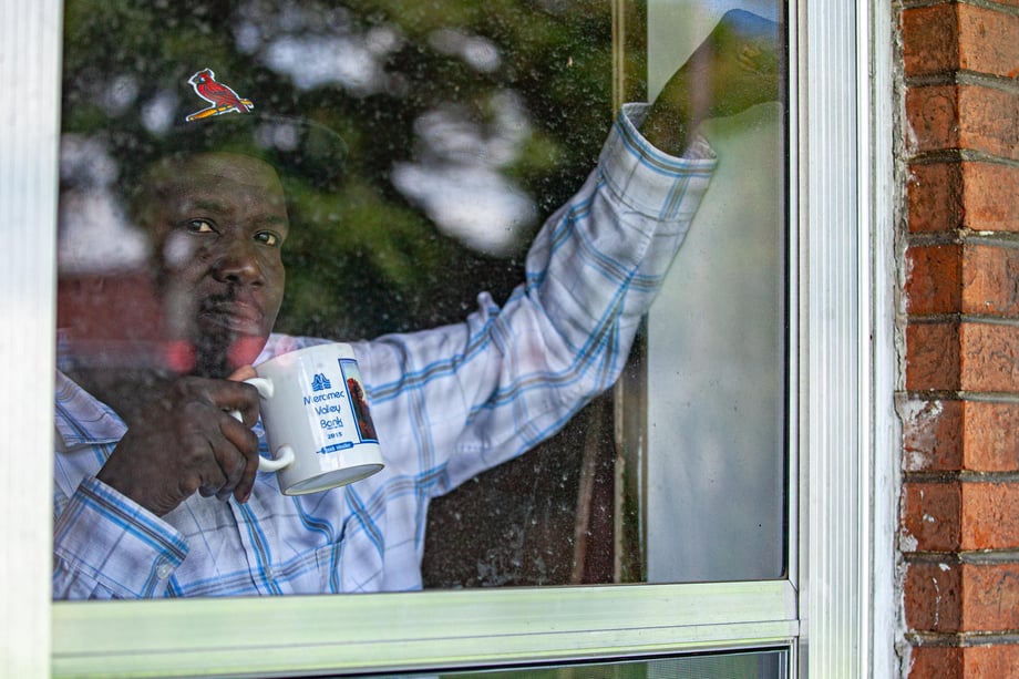 Photo by Lou Bopp of neighbor looking out his window with a coffee and a Cardinals hat on.