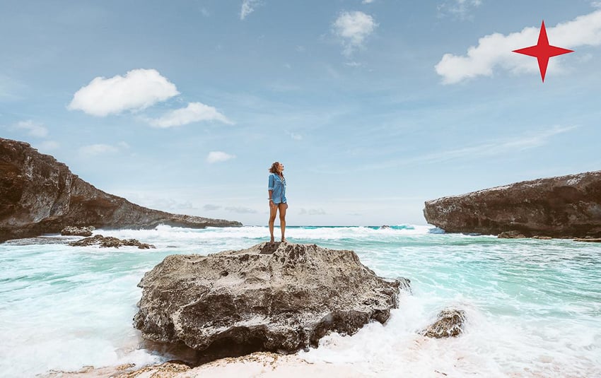 Myles McGuinness captures a photo of a woman standing on  arock looking at the view in Aruba