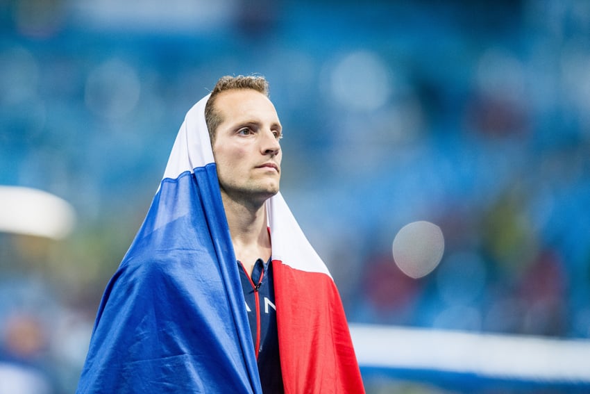 An athlete standing surrounded by his flag shot by Alex Buisse.