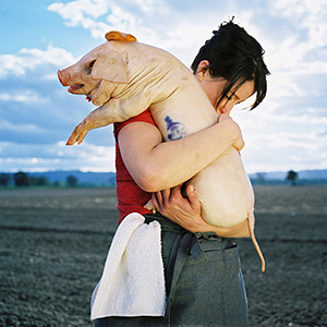A photo of a chef hugging a dead pig in an open field by Alicia J. Rose for Elle Magazine.