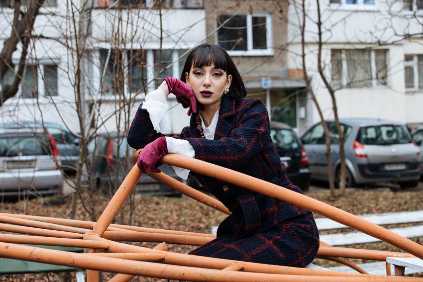 a model in a navy suit and pink gloves on a vintage playground structure in Bulgaria