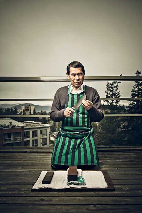 Photograph of a man sharpening a knife with whetstones and wearing a green and black striped apron, taken by Carlo Ricci