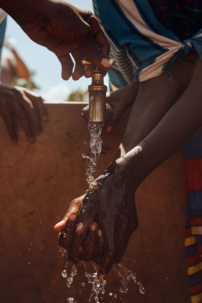 Clay Cook photographs a Maasai member running hand through clean water.