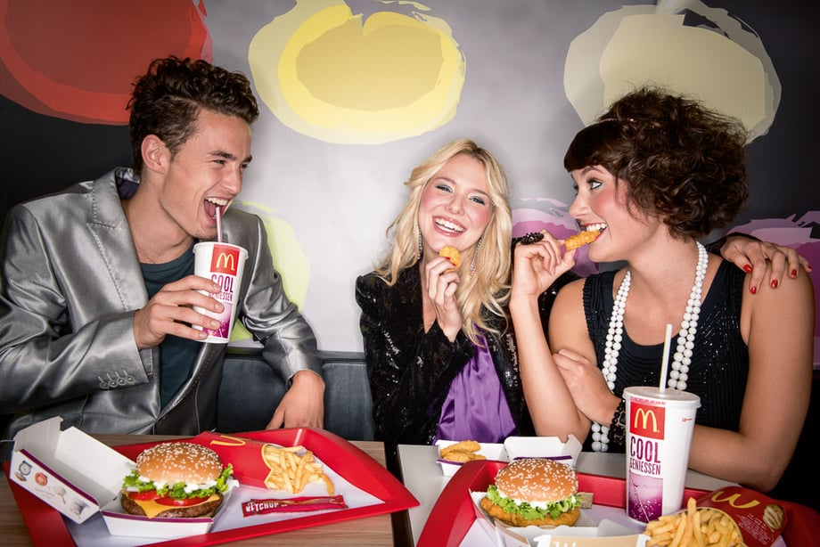 Three friends smiling as one sips a soda and the others share chicken nuggets shot by Munich-based lifestyle photographer Christian Brecheis for McDonald's