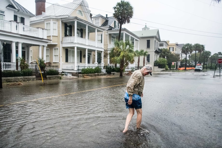 Sean Rayford photographs a man in shorts and bare feet wading through water on a flooded street in Charleston