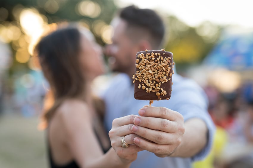 Photo by Kevin Brown for the State Fair of Texas of a couple about to kiss, holding an ice cream bar towards the camera as if to hide behind it.
