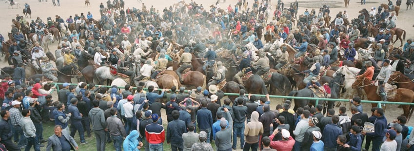 Buzkashi players swarm near an onlooking crowd by Marc Ressang