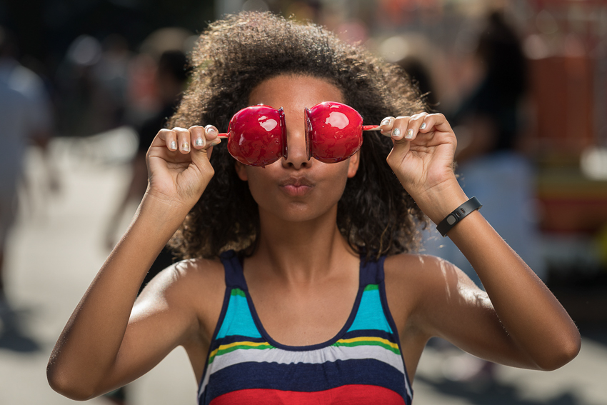 Photo of a girl holding two candied apples in front of her eyes and making a face.