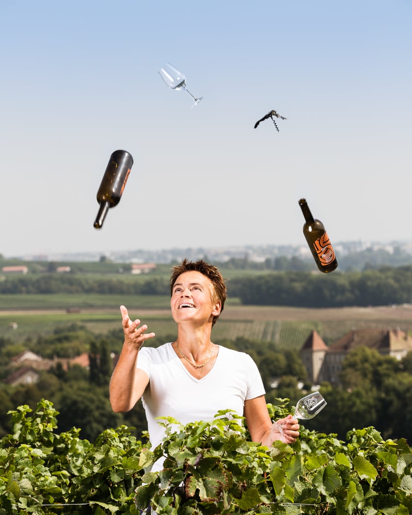 Portrait of Sophie Dugerdil juggling bottles of wine and wine glasses.