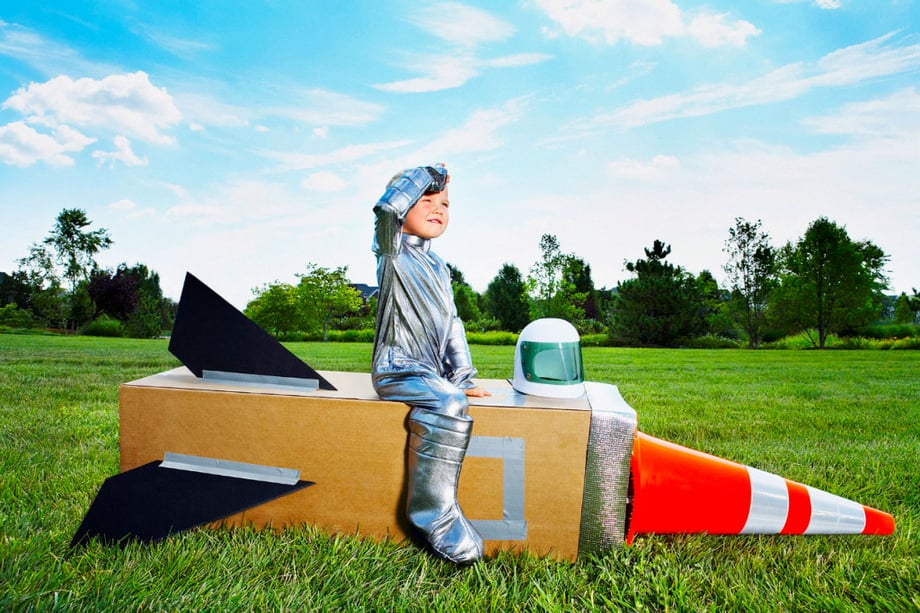 kids photography; a little boy in a silver space suit sitting on a rocket ship made out of cardboard and a traffic cone