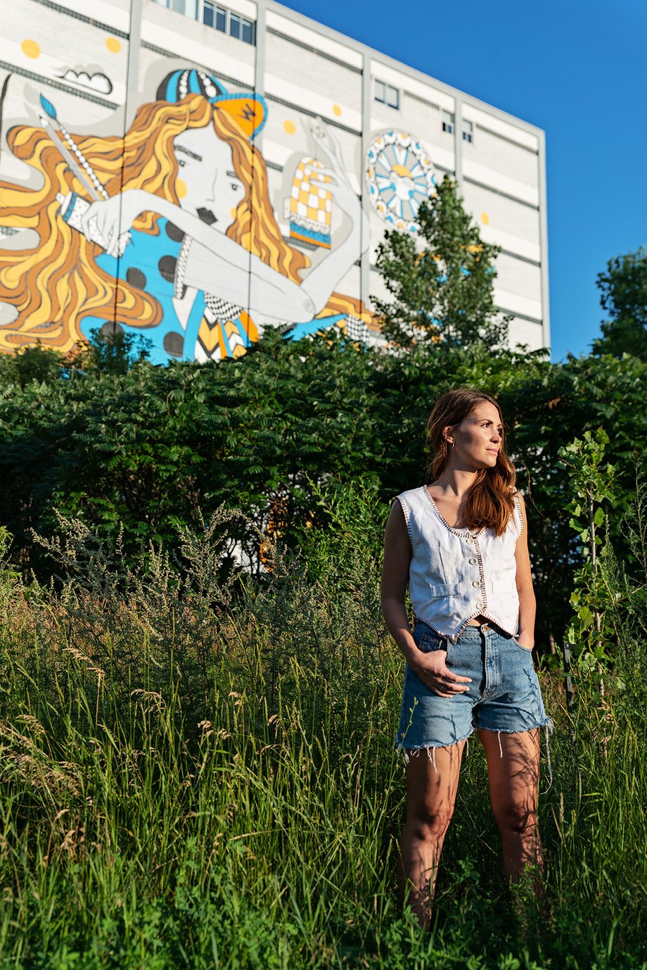 Brittany stands in front of greenery and another mural in Mile End in this photo by David Giral