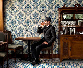 Man drinking in a dining room photographed by Erin Kunkel