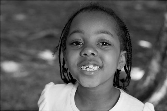 Black and white portrait of a young child smiling at the camera captured by Kevin Brusie for Flashes of Hope.