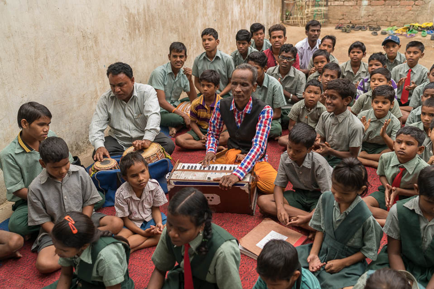 Students listening to their teachers perform a song on drums and keyboard, photo by Gary Chapman