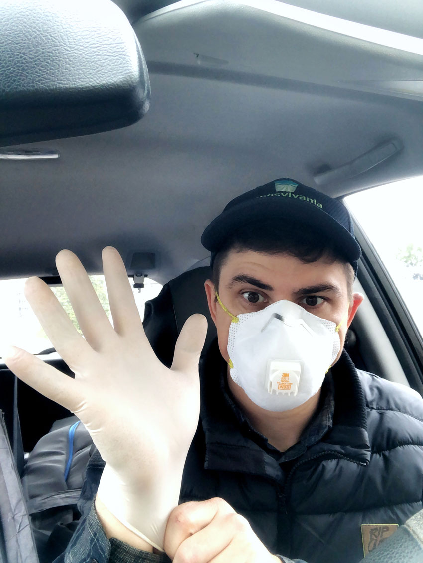 Photo of Gene Smirnov wearing a mask and gloves behind the wheel of his car.