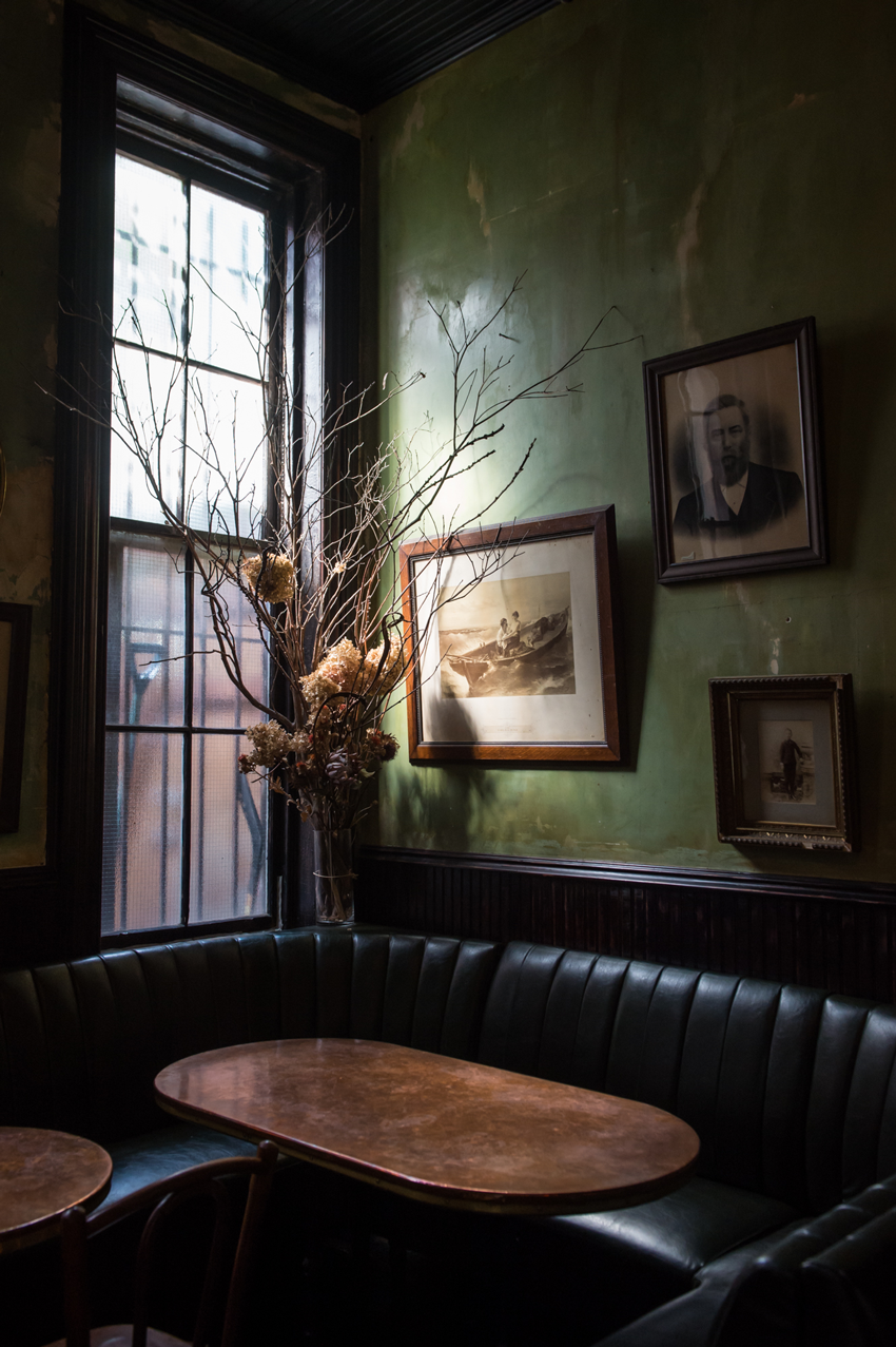A dark, cozy booth in the corner of a dimly lit bar, with vintage photos artistically hanging on the wall, photo by Jennifer May