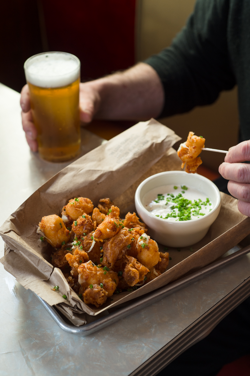 A man is enjoying a cold beer and a delicious fried appetizer, photo by Jennifer May.