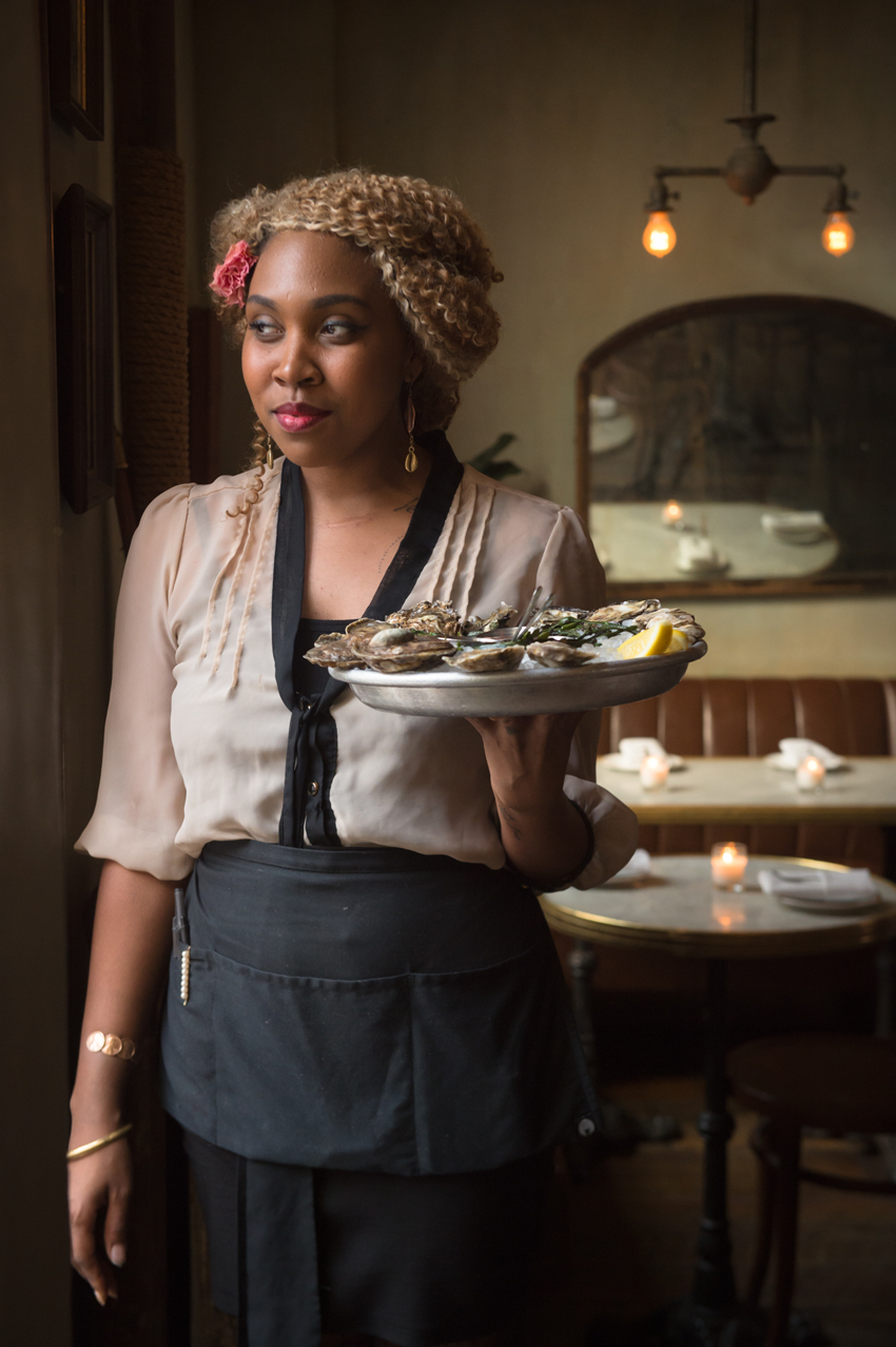 A nicely dressed server brings out a plate of fresh oysters over ice, photo by Jennifer May. 