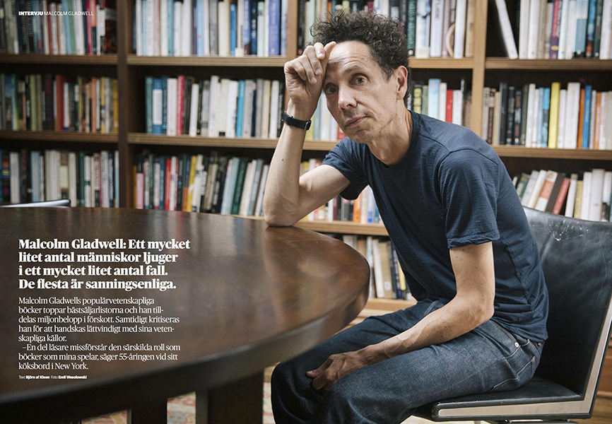 Photo of Malcolm Gladwell looking up from a table in front of a wall of books.