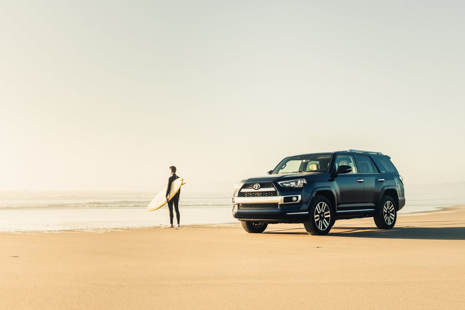 A surfer walks into the ocean with his board while his Toyota 4Runner is parked on the beach, photo by Mark Skovorodko