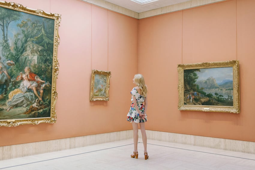 Photo by Megan Taylor of a woman standing in an art museum looking a paintings.